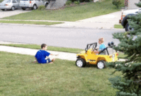 Boy runs over another boy on a lawn in a Power Wheels truck.