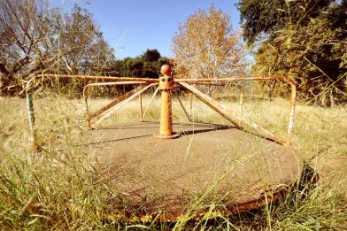 Photo of an old, rusting playground roundabout.