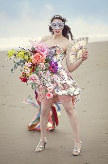 Photo of lady wearing floral dress and holding a large bunch of flowers on a beach.