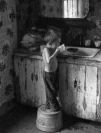 A boy sips at a cup in darkened kitchen.