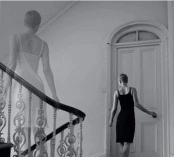 A woman looks back on a stairway and sees an image of herself.